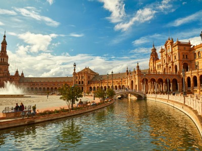 Plaza de España in Sevilla met kanaal, brug en fontein onder blauwe lucht.