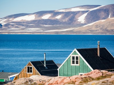 Groen en houten huis aan de kust met uitzicht op fjord en besneeuwde bergen op de route vier Arctische eilanden.
