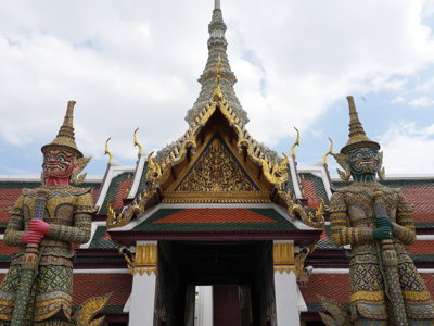 Poort van het Grand Palace in Bangkok met twee kleurrijke tempelwachters en rijk versierde dakrand.