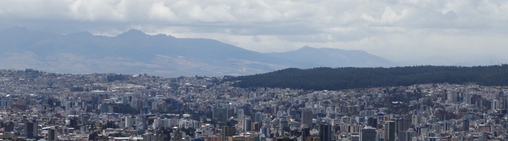 Panoramisch uitzicht over Quito met de stad tussen bergen en wolkenlucht.