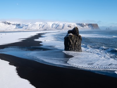 Zwart zandstrand bij Vik in IJsland met basaltrots in zee, omringd door sneeuw en winterse golven.