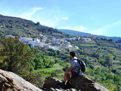 Wandelaar met rugzak kijkt uit over een wit bergdorp in de Sierra Nevada bij Granada.