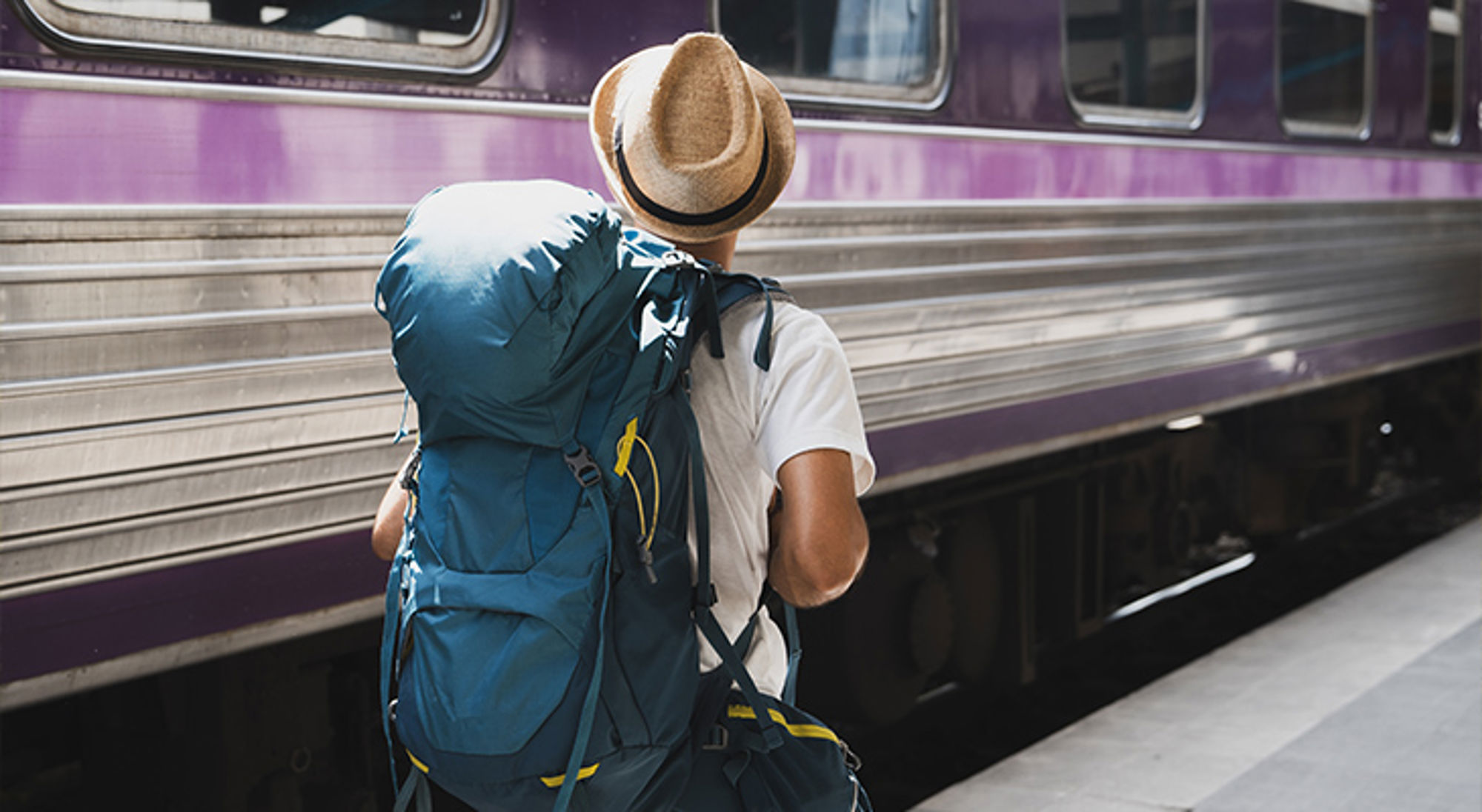 Reizen met een backpack Backpacker met grote rugzak en hoed op een perron naast een trein.