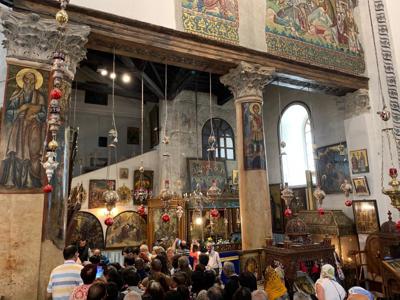 Interieur van een kerk in Israël met iconen, zuilen en hangende lampen, terwijl bezoekers rondkijken.