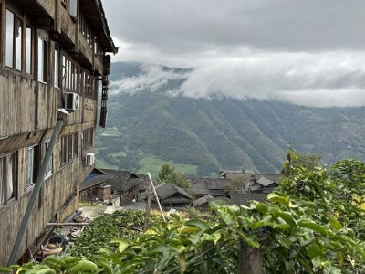 Houten dorpshuizen met uitzicht op groene bergen en laaghangende wolken langs de Route China.