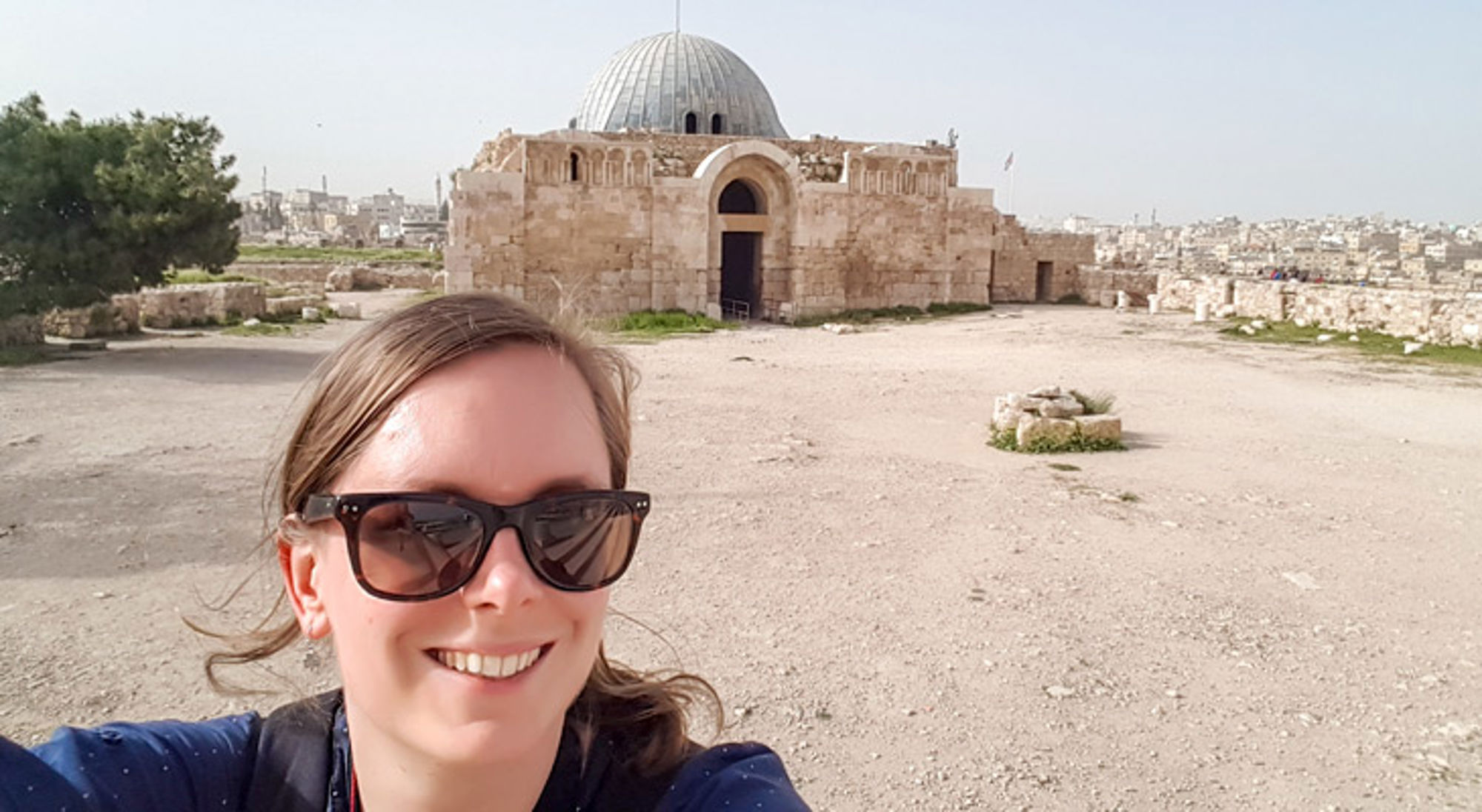 Selfie bij een historisch stenen gebouw met koepel, met uitzicht over de stad op de achtergrond.
