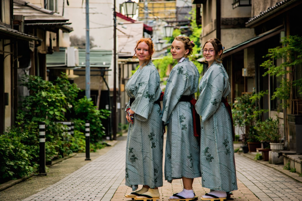 Drie meisjes in yukata op een rustige straat in Japan tijdens een familiereis.
