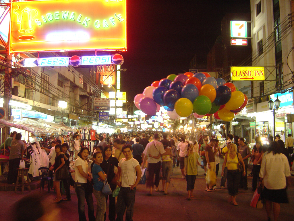 Drukke avondmarkt in Bangkok met neonreclames en kleurrijke ballonnen.