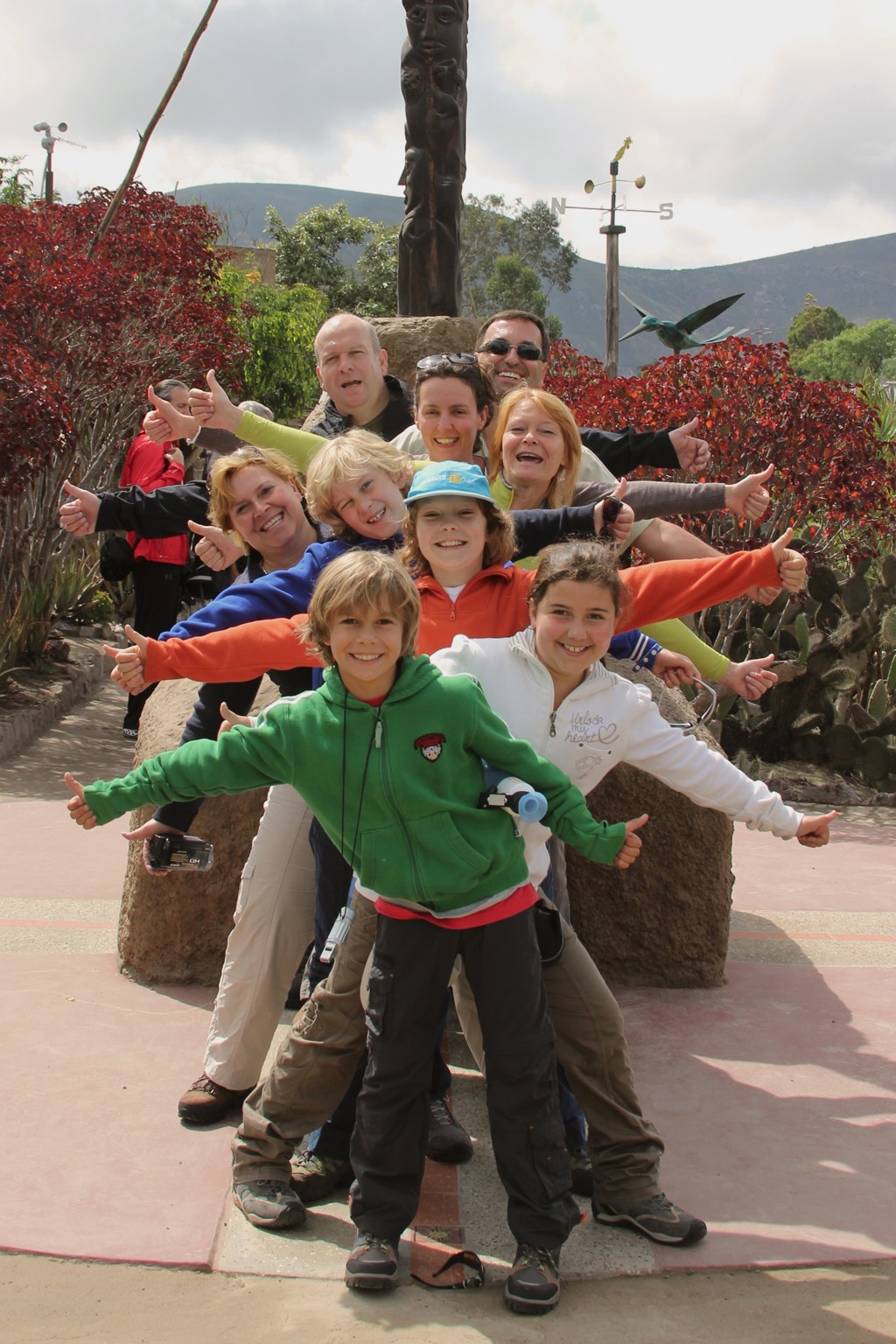 Groep gezinnen poseert met gespreide armen tijdens familiereis Ecuador en Galapagos, met bergen op de achtergrond.