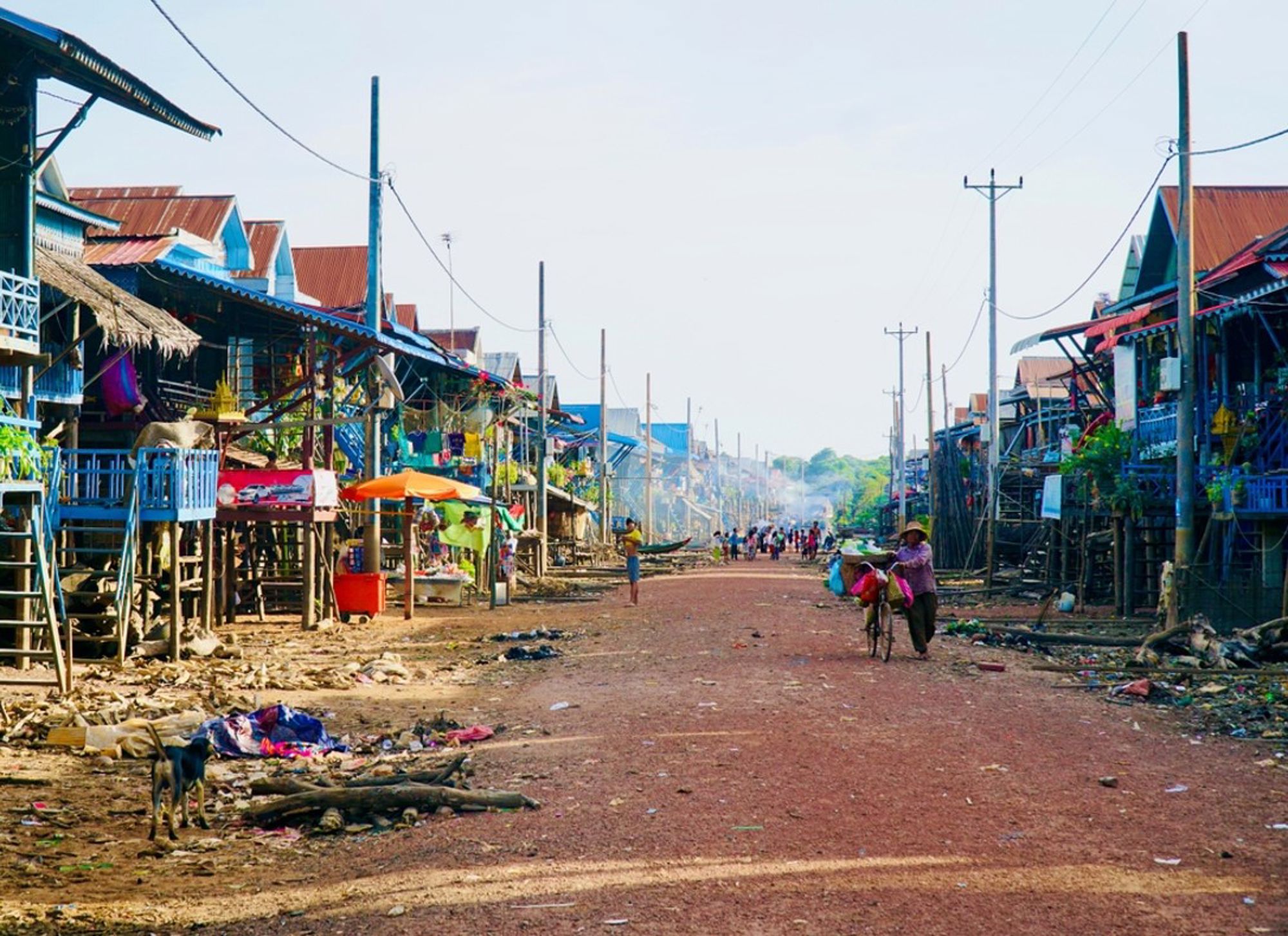 Stofstraat met paalwoningen en marktstalletjes in een dorp in Cambodja.