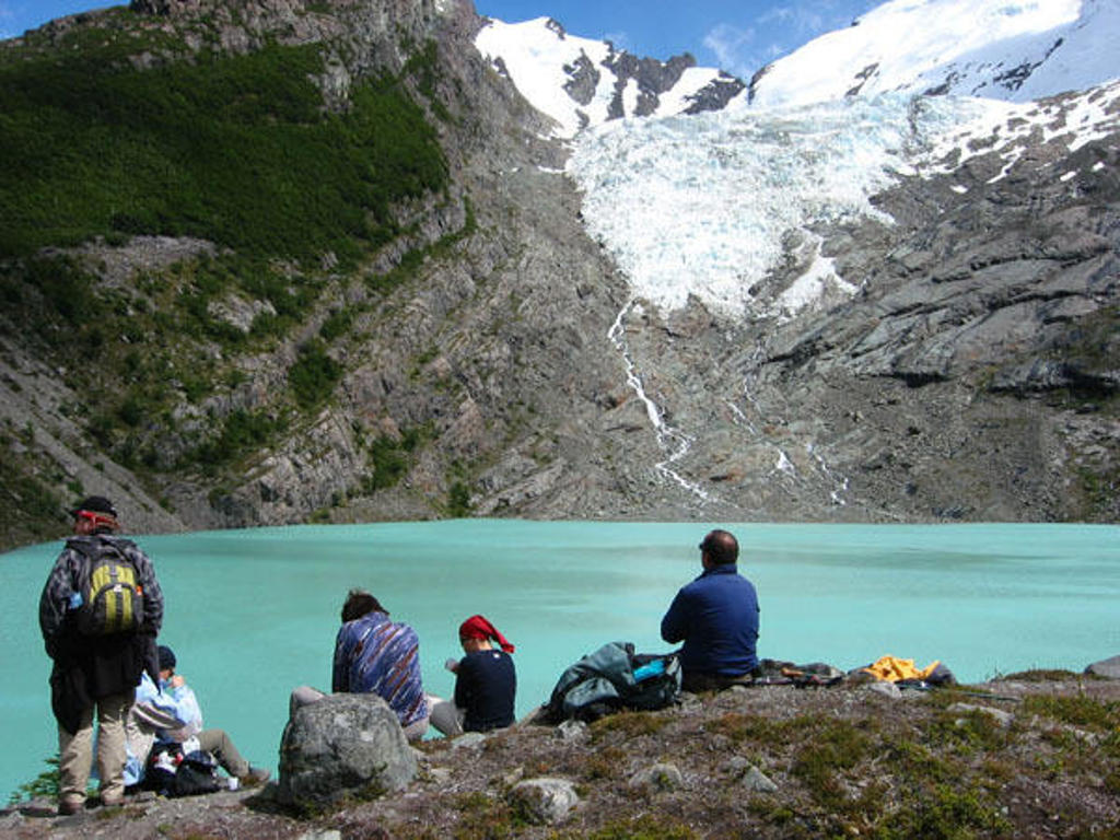 Wandelaars bij een azuurblauw gletsjermeer met besneeuwde bergtoppen in Patagonië.