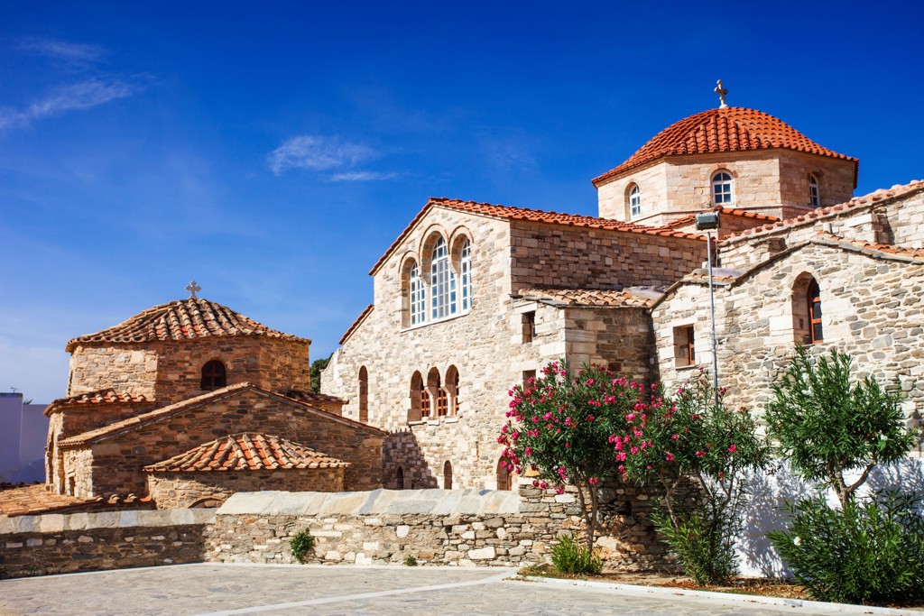 Byzantijnse stenen kerk met rode koepels op Naxos, Griekenland, onder een strakblauwe lucht.