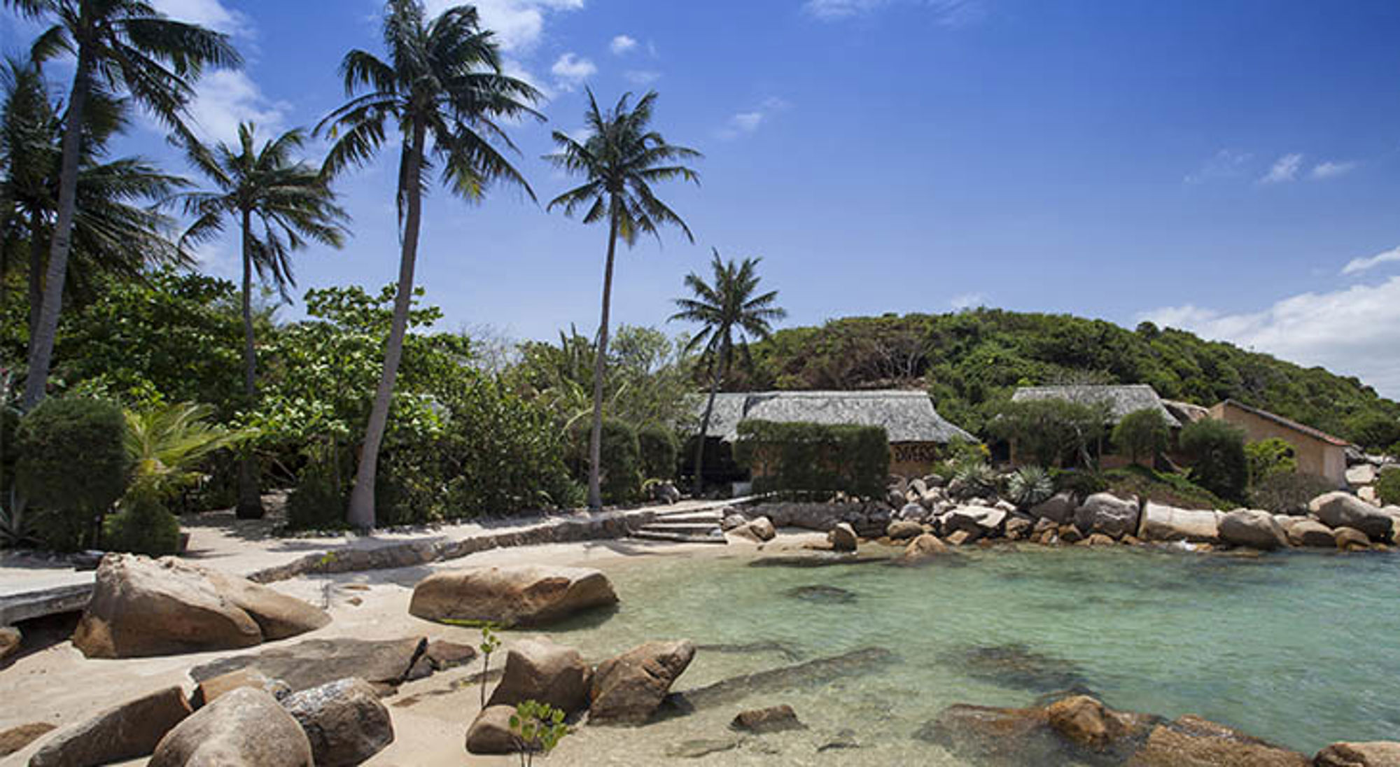 Whale island Tropisch strand in Vietnam met palmbomen, rotsen en helderblauw water bij bungalows aan de kust.
