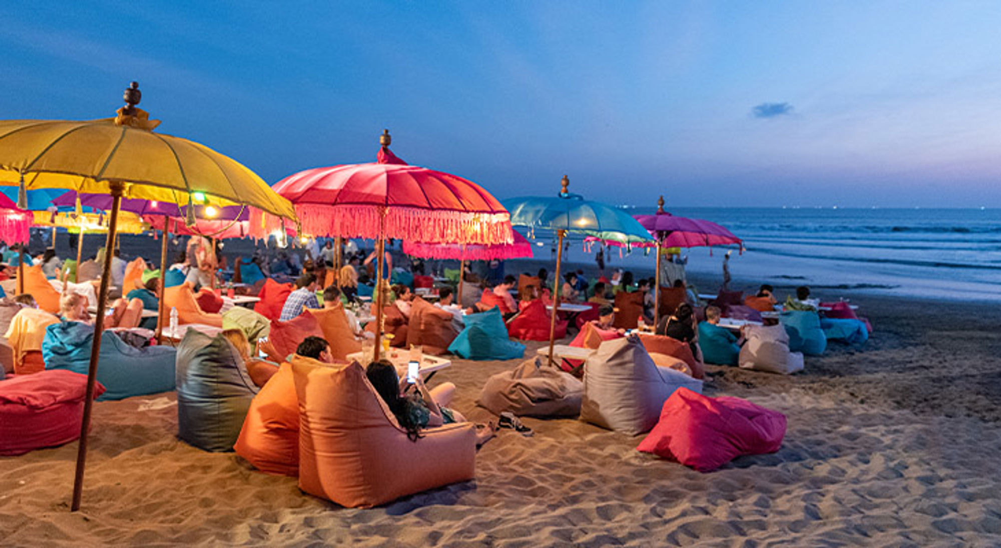 Kuta Beach Bali Kleurrijke strandbar bij zonsondergang met zitzakken en parasols aan zee.