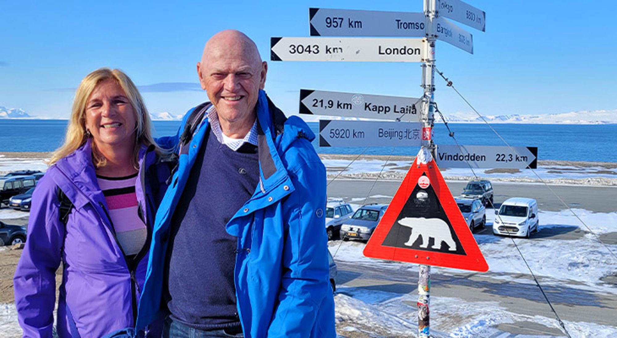 Ageeth en haar man Twee reizigers bij wegwijzers en waarschuwingsbord voor ijsbeer in een besneeuwd kustlandschap.