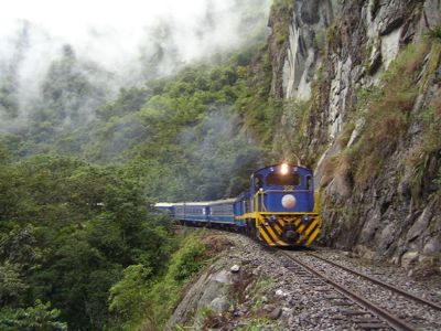 Blauwe trein rijdt langs steile rotswand door mistig Andeslandschap in Peru.