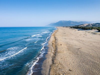 Lang zandstrand aan de Turquoise Kust in Turkije met golven en bergen op de achtergrond.