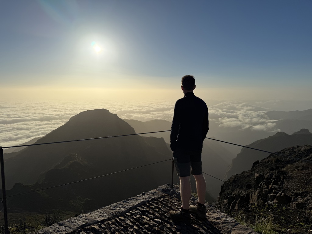 Wandelaar kijkt uit over bergtoppen en zee van wolken op Madeira tijdens een wandelvakantie.