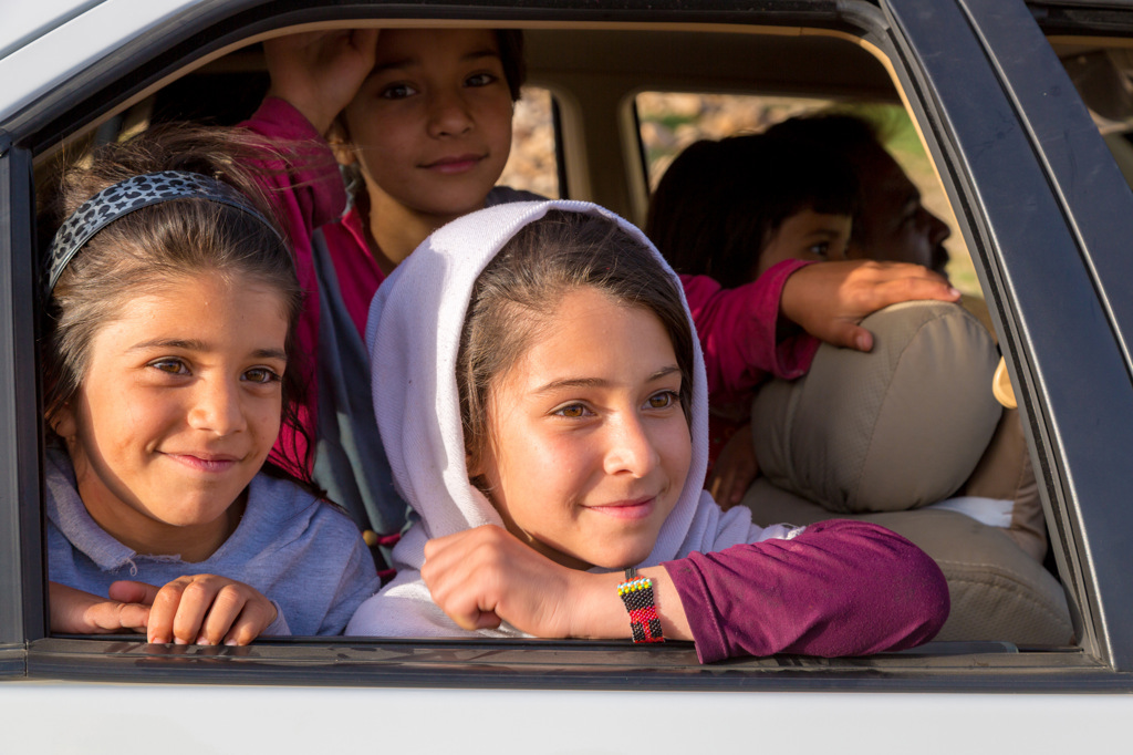 Lachende Iraanse meisjes kijken uit het autoraam tijdens een groepsrondreis door Iran.