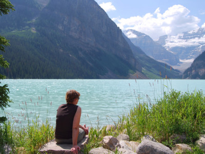Reiziger aan de oever van Lake Louise in Canada, met turquoise meer en besneeuwde bergen op de achtergrond.
