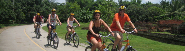 Groep fietsers met helm op een weg door groen landschap in Thailand.