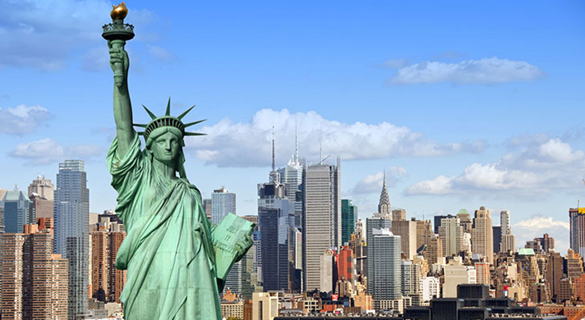 Vrijheidsbeeld met skyline van Manhattan in New York onder een blauwe lucht.