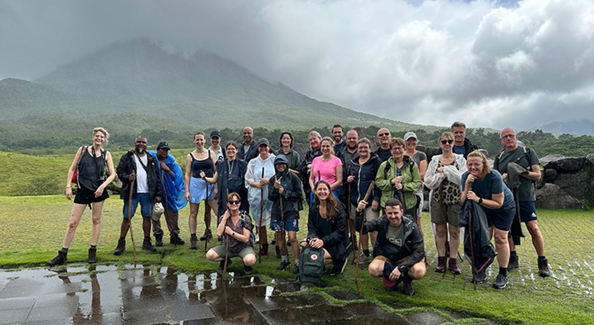 Costa Rica in het regenseizoen Groep wandelaars poseert met wandelstokken in groen landschap met berg op de achtergrond.
