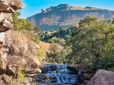 Waterval in de Drakensbergen met rotswanden en groen dal langs de route Johannesburg–Kaapstad.
