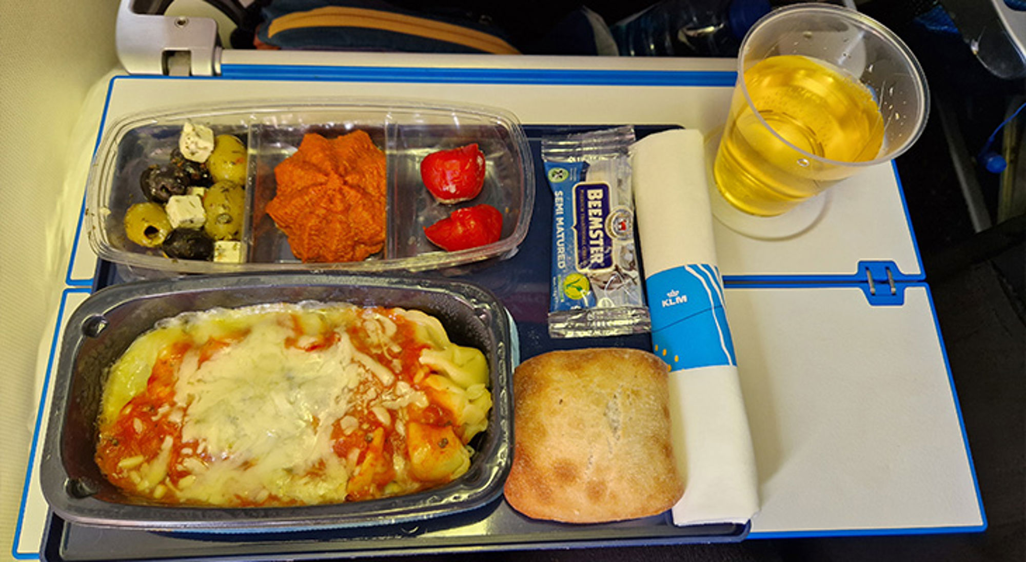 KLM maaltijd KLM vliegtuigmaaltijd met pasta, broodje, olijven, kaas en een glas drank op het uitklaptafeltje.