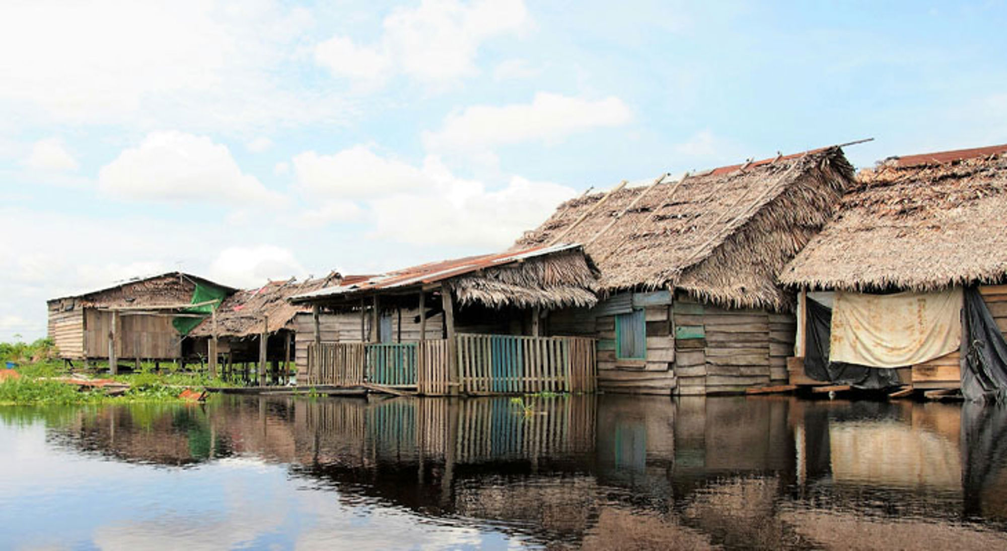 Iquitos Houten huizen op palen langs het water in Peru, met rieten daken en weerspiegeling in de rivier.