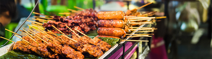 Gegrilde streetfoodspiesjes en worstjes op een marktstalletje.