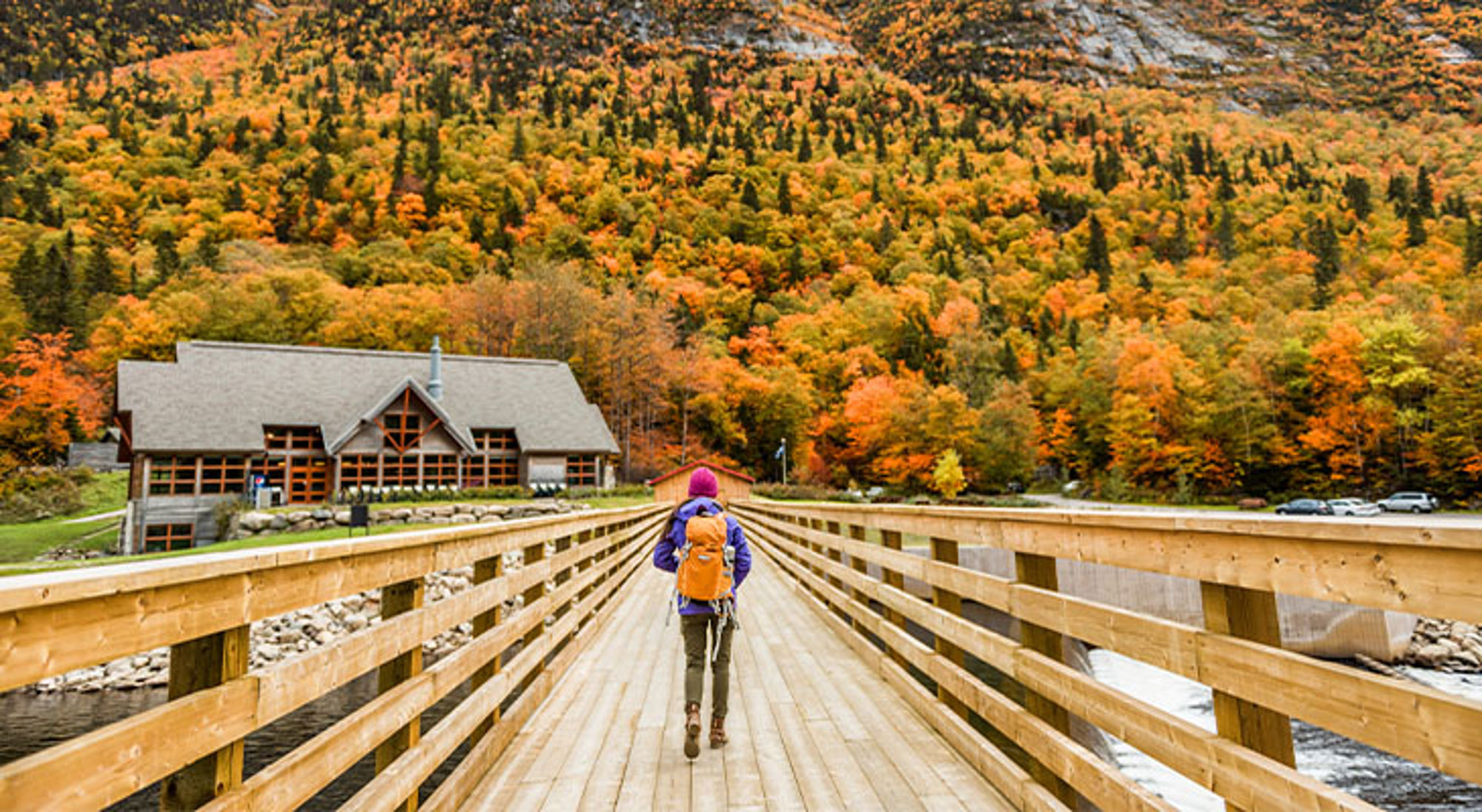 Quebec, Canada Wandelaar met rugzak op houten brug richting lodge, met kleurrijk herfstbos op de achtergrond.