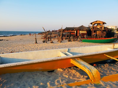 Traditionele vissersboot op het strand van Madagascar bij zonsondergang, met strandhutten en de zee op de achtergrond.
