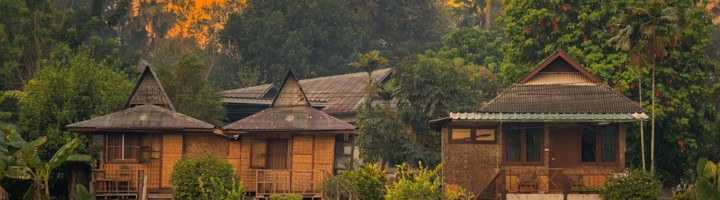 Houten huisjes in het groen bij Pai, Thailand, met zonsondergang op de achtergrond.