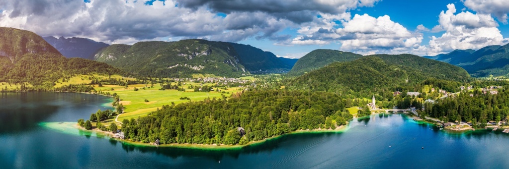 Panorama van het Meer van Bohinj in Slovenië, met groene bergen, bossen en helderblauw water.