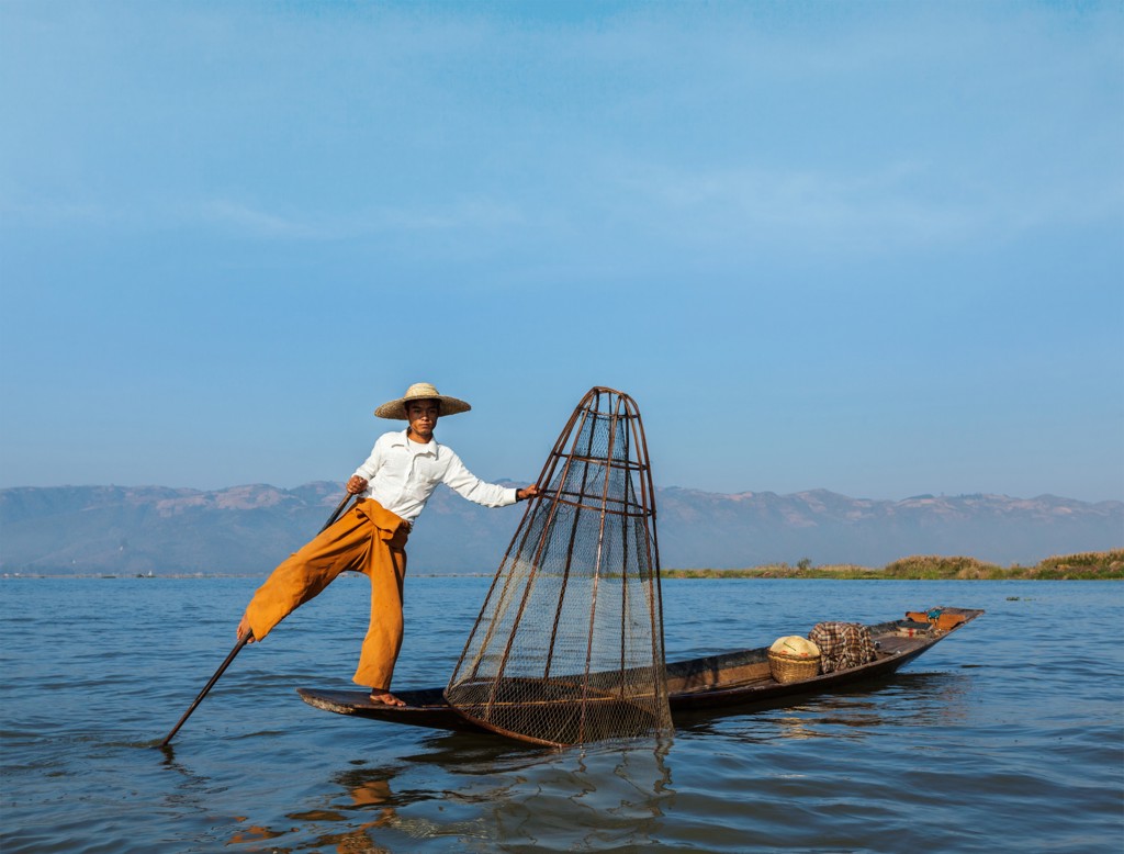 Visser op Inle Lake in Myanmar balanceert op één been in een boot met traditioneel visnet.