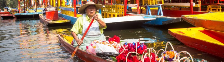 Bloemenverkoper in boot tussen kleurrijke trajineras op de kanalen van Xochimilco, Mexico.