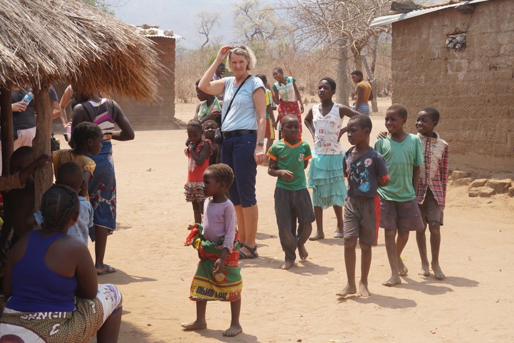 Reiziger tijdens groepsrondreis Zimbabwe in een dorp, omringd door spelende kinderen bij lemen huizen.