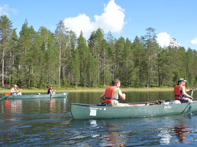 Kanotocht op een meer in Lapland, langs een groen naaldbos onder een blauwe lucht.