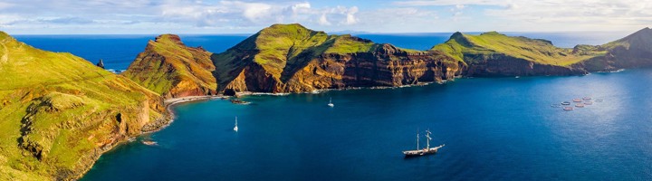 Groene kliffen en bergkammen aan de kust van Madeira met zeilboot op zee.