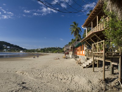 Strand aan de Pacifische kust van Nicaragua met palmbomen en strandlodges langs het zand.