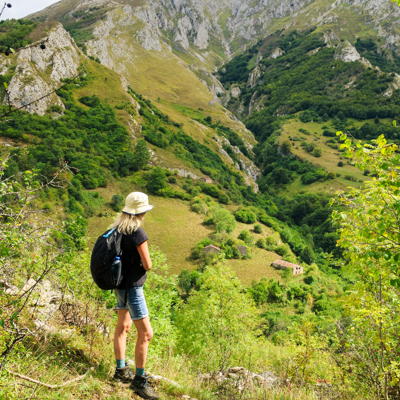Wandelaar met rugzak kijkt uit over groene bergvallei in de Picos de Europa, Spanje.