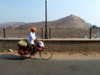 Fietser met bagage langs een meer met heuvels op de achtergrond, route India en Nepal 21 dagen.