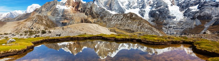 Besneeuwde pieken van de Cordillera Huayhuash met weerspiegeling in een bergmeertje, Peru.