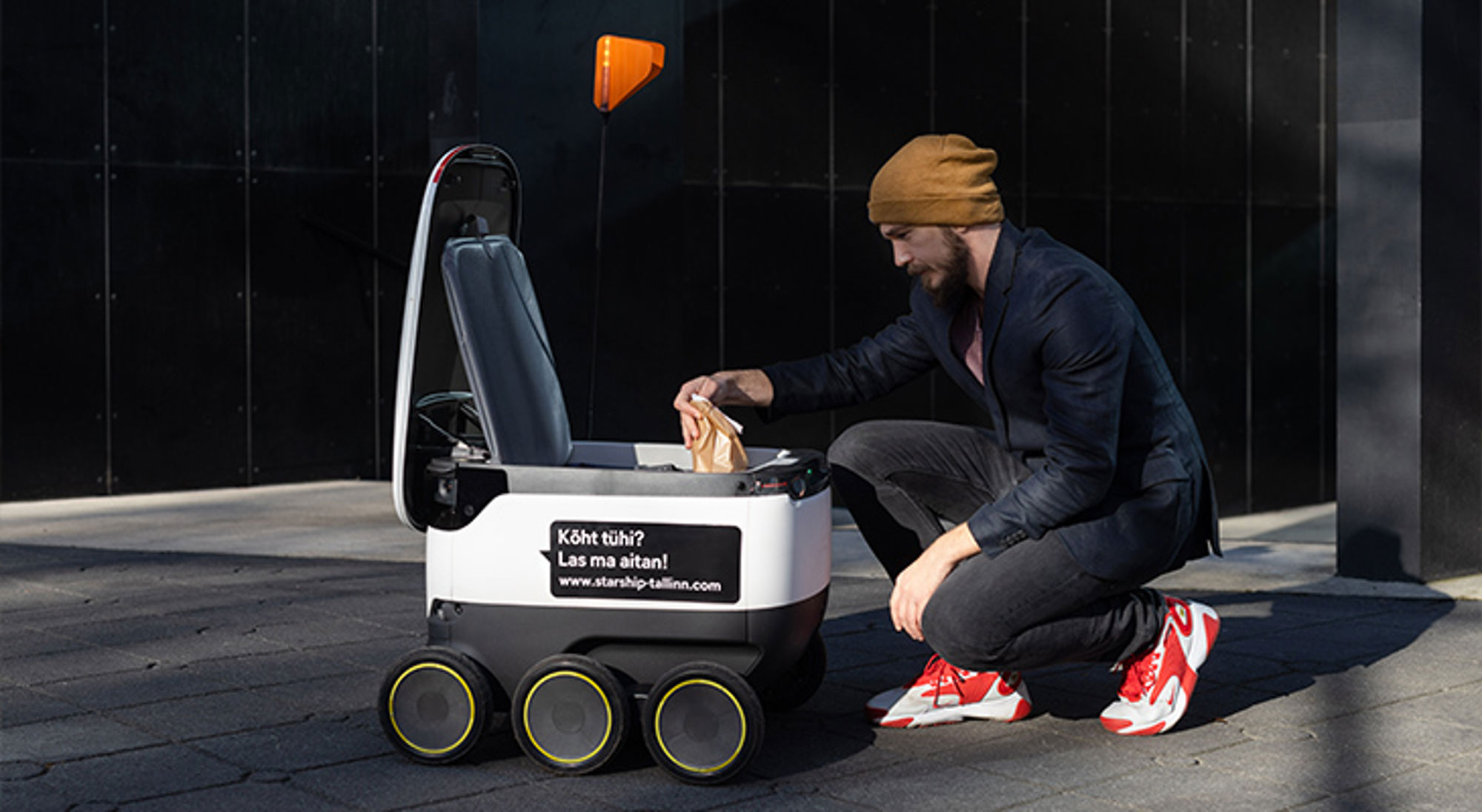 Robot bezorger Man knielt bij bezorgrobot en pakt een papieren zak uit het open vak.