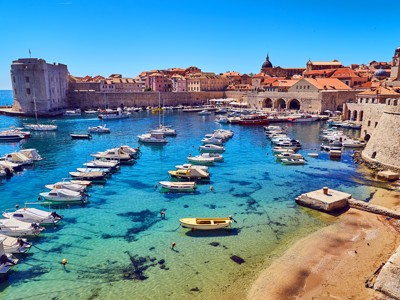 Haven van Dubrovnik met oude stadsmuren en bootjes in helderblauw water.
