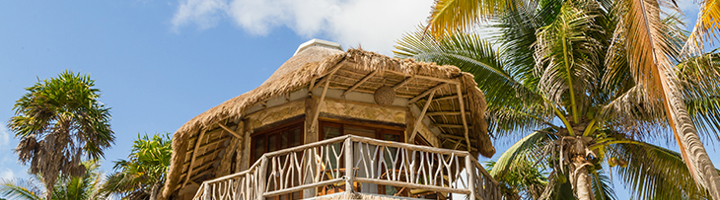 Rieten strandlodge met balkon tussen palmbomen, bijzondere overnachting tijdens een Sawadee reis.