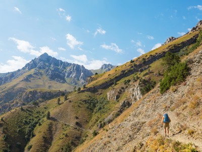 Wandelaar op bergpad in de Oezbeekse bergen tijdens Route Oezbekistan, met ruige pieken en groene hellingen.