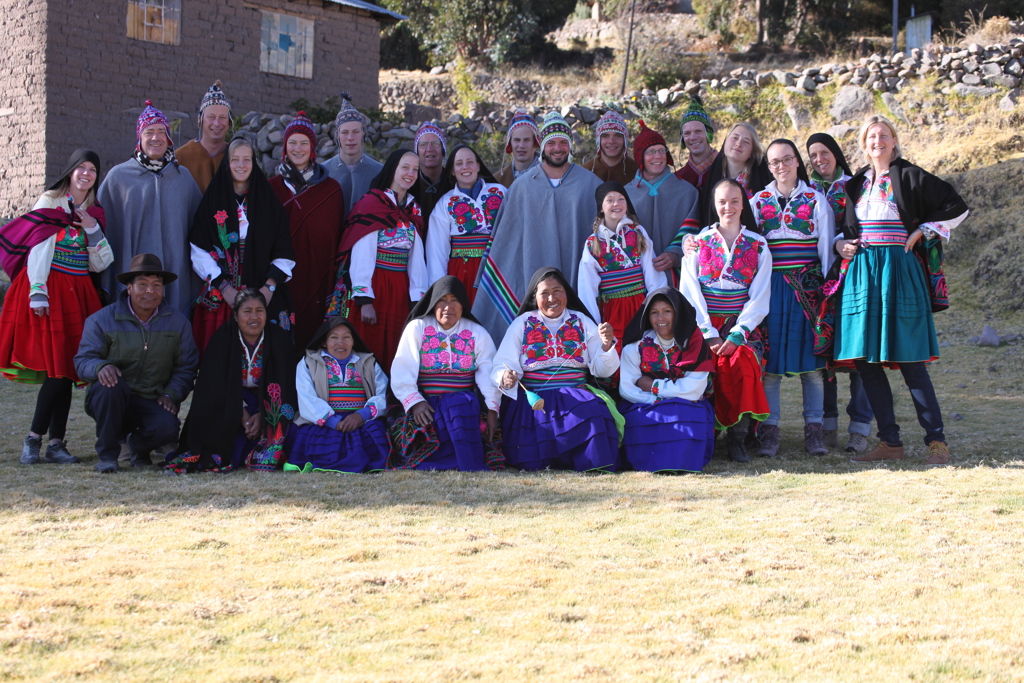 Groepsfoto tijdens familiereis Peru met locals en reizigers in kleurrijke traditionele kleding in een bergdorp.