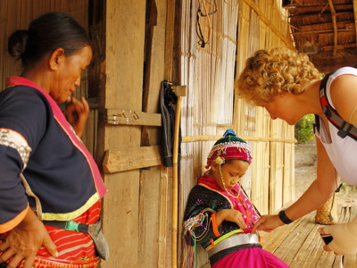 Toerist in Thailand maakt contact met een kind in traditionele kleding bij een houten huis.